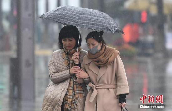 资料图：11月27日，两位市民着冬装雨中出行。中新社记者 王刚 摄