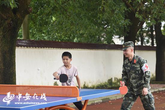 2020年7月21日，安徽铜陵，在安徽省铜陵市义安区太平中心小学防汛安置点，武警合肥支队医疗小分队卫生员跟一对留守双胞胎男孩打乒乓球。
