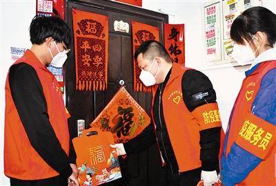 图为防疫服务员将“福”字文化礼包挂在居民家门把手上。
