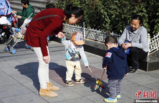 资料图:北京街头两名孩子在母亲的带领下玩耍。中新社发 张浩 摄