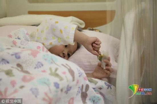 2018年11月17日，北京，躺在病床上的小娅馨正在玩耍手中的鲜花。魏建顺/视觉中国
