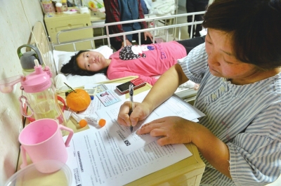 小琴躺在病床上轻微抽搐，妈妈在一旁填写申请表希望能够得到资助给女儿看病。京华时报记者王海欣摄