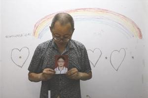 邓虎成手持女儿照片希望她回来，墙上是女儿画的彩虹、爱心