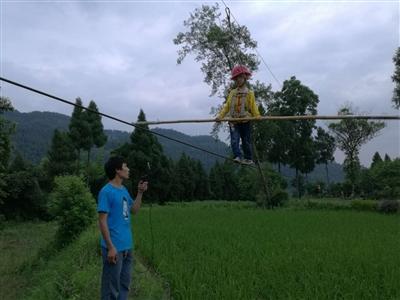 在张禹的练习下,望望戴着安然帽,端着竹竿,在河堤钢丝上行走。