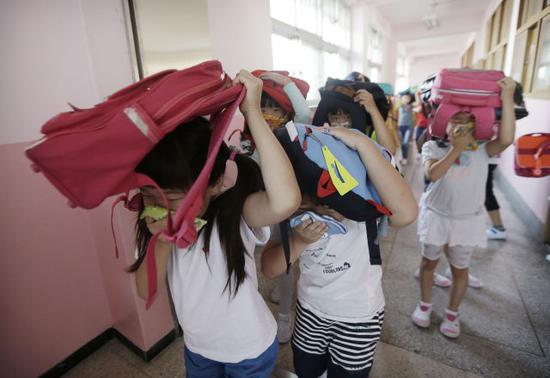 2016年9月23日，在韩国首尔，一所小学的学生在地震演习中头顶书包逃出教室。（新华/美联）