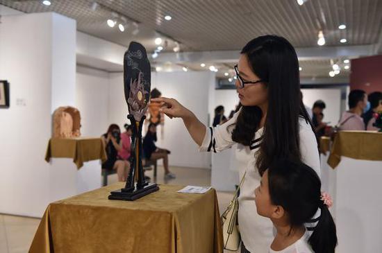 展览现场,一位母亲正在给女孩讲解皮雕上的图案