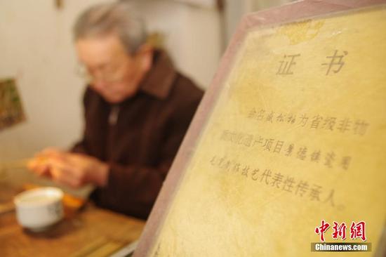 老人的工作台边，放着一块由江西省文化部门颁发的“非物质文化遗产传承人”证书，每天早上他来到店内，先仔细将这块证书擦一遍，再开工制笔。 王昊阳 摄