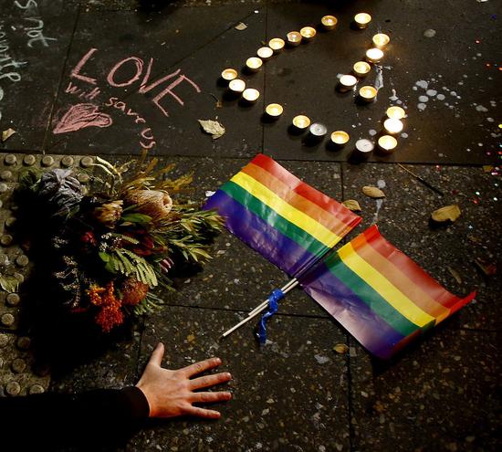 6月13日，澳大利亚悉尼。一名男子在为枪击案遇难者祈福活动中，将手放在了彩虹旗旁。
