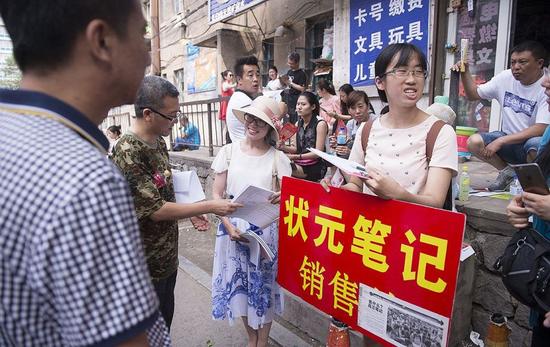 资料图片：6月28日，长春市，一中考考场外，六位今年的高考生举牌销售“状元笔记”，贩卖考试成功学。