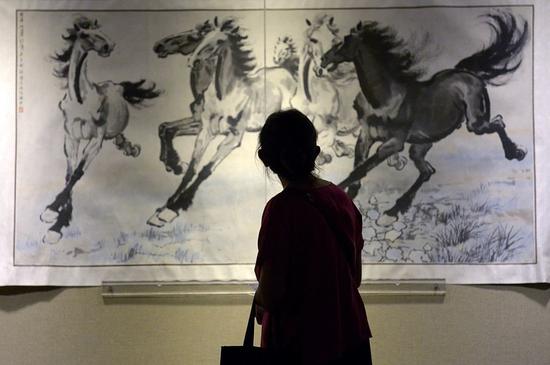 2014年6月26日，一位观众在北京的一家博物馆观看徐悲鸿的《奔马图》（Six Galloping Horses ）。著名国画大师徐悲鸿在抗战期间使用简单有力的笔法绘制的奔马图，意在鼓励人民在战争中坚强振作。这些画现在都已价值连城。图片：Courtesy of WANG ZHAO/AFP/Getty Images