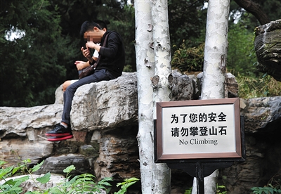 10月2日，景山公园，两名游客坐在假山上，对一旁竖立的“请勿攀登山石”牌子视而不见。