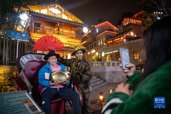 在重庆“十八梯”老街，游客坐在黄包车上与装扮成铜像的演员合影（12月9日摄）