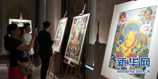 “五彩祥云——西藏唐卡艺术重庆首展”现场,游客拿出手机拍摄唐卡作品。新华网发(主办方供图)