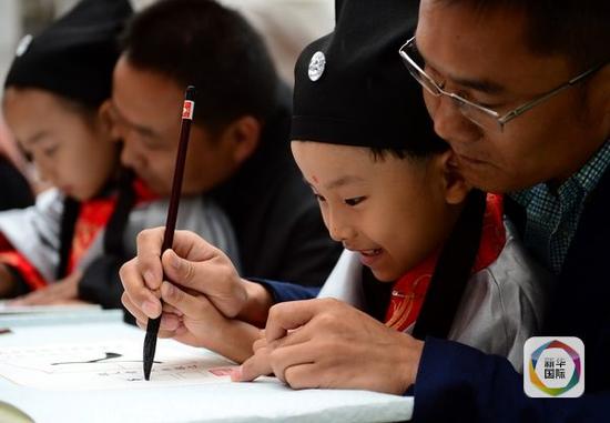 资料：2014年9月1日，兰州市七里河小学一名学生在家长的帮助下用毛笔书写“人”字。（新华社记者 张锰 摄）
