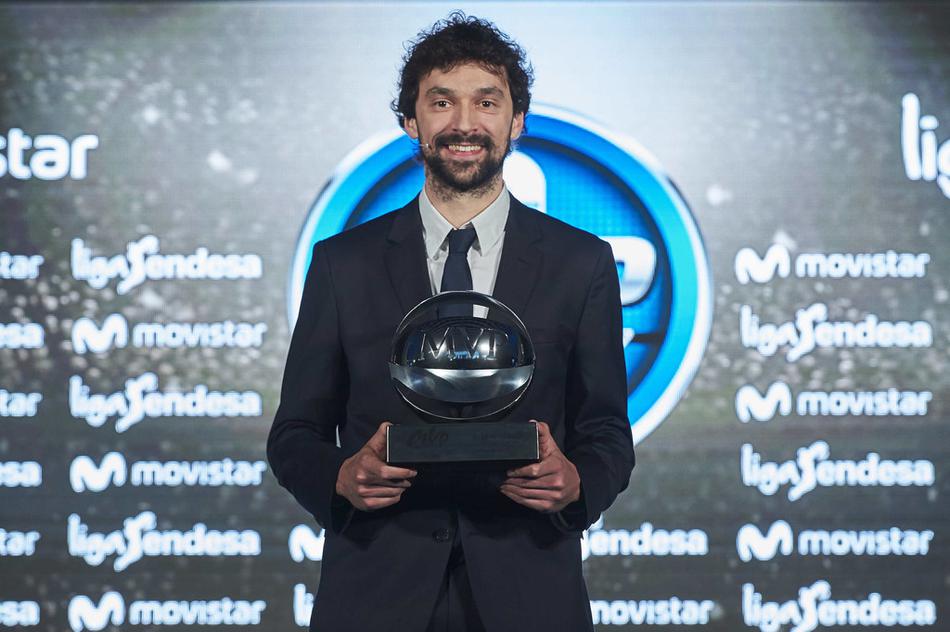 鲁尔手捧西甲MVP奖杯，腼腆的笑容里藏着杀手本色，身后的皇马队旗见证了他这一赛季的传奇。