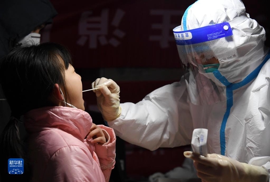12月25日晚，在西安市莲湖区劳动路核酸采样点，医务人员为小朋友进行咽拭子采样。新华社记者 李一博 摄