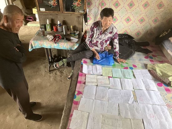建華鎮雙勝村一對老夫妻將近幾年收到的關於土地的文書鋪在炕上給記者展示，其中既有承包合約、驗收證明，也有禁墾告知書，行政處罰決定書。