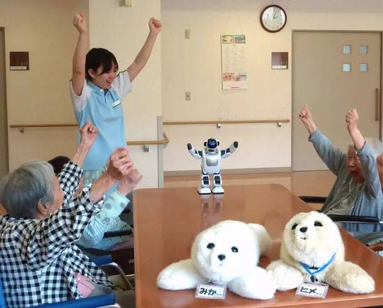 2013年6月11日,日本横滨一家养老院内,老人们与仿生机器人互动。