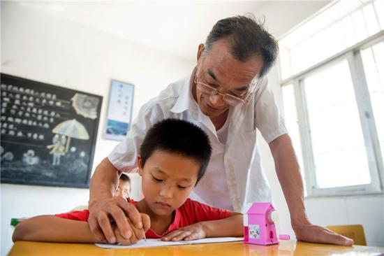 2015年9月8日,在安徽省六安市金寨县梁山小学内,返聘老师叶乃合在给一名孩子辅导作业。新华社记者 郭晨 摄