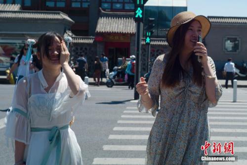 5月21日,北京天气晴晒,两位姑娘走过人行横道。 中新社记者 盛佳鹏 摄
