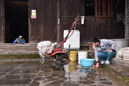 石欣在屋外冲洗自家养殖的黄鳝,儿子趴在门槛上叫爸爸。