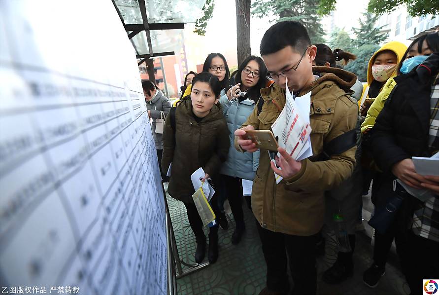 10年来，摄影师连续记录国考，这期间感受到的除了人山人海赶考场景外，还有考场外埋头充电，迟到当场落泪……这些影像中展现的，不仅仅是考生漫长而艰辛考试路，还有考生对公务员职业的期待。图为2017年12月10日早晨，国考安徽合肥庐阳中学考点，考生在查看考场位置。江雨/摄影