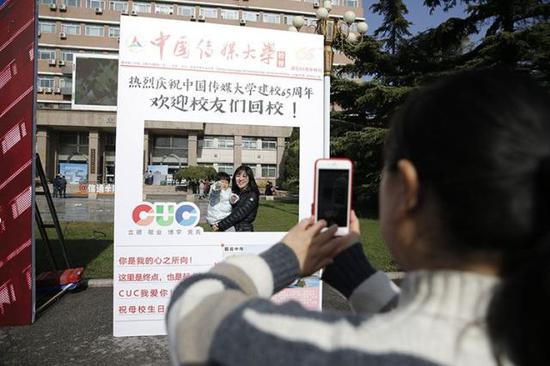 中国传媒大学迎来65周年校庆,校友们在纪念板前拍照留念。