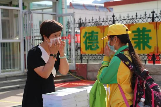 在学校门口,王春艳校长为每个返校的学生赠送健康礼包,并为孩子演示正确佩戴口罩的方式。