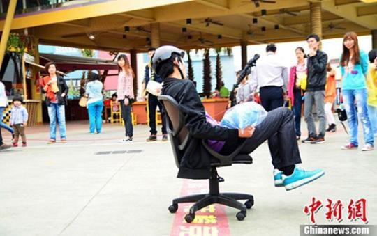 2013年，3月30日，西方愚人节即将来临，武汉欢乐谷上演了一场极具趣味性的“娱乐减压旋转椅竞速大赛”。参赛游客坐在办公旋转椅上，身体不离椅子，运用脚的力量，旋转着向目的地极速出发。比赛以两人一组接力进行，游客们纷纷上阵参与，“娱”乐愚人节。中新社发 胡芬 摄