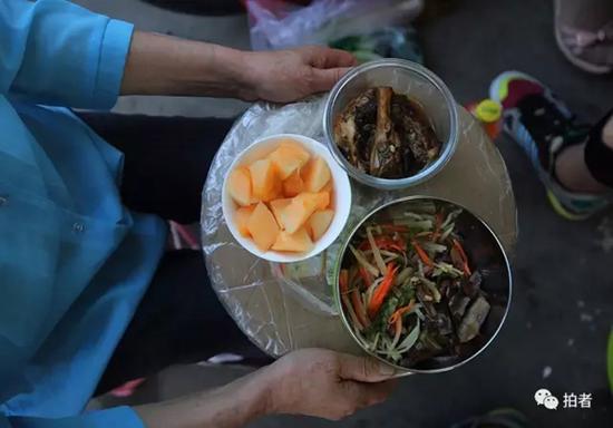 6月2日，毛中东门，65岁的姜奶奶用圆纸板端着两道菜和一盒水果，等着孙子夹菜，每天老人要送两次饭。