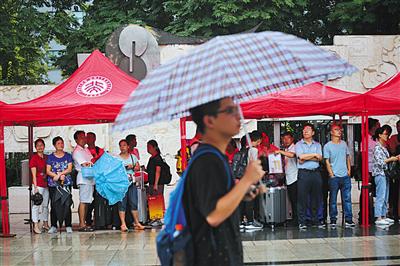 昨晨北京下起小雨，陪同报到的家长们在雨棚下避雨。