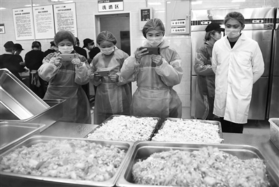 ◀朝霞小学学生家长义务监督员在学校食堂内拍摄饭菜制作过程。