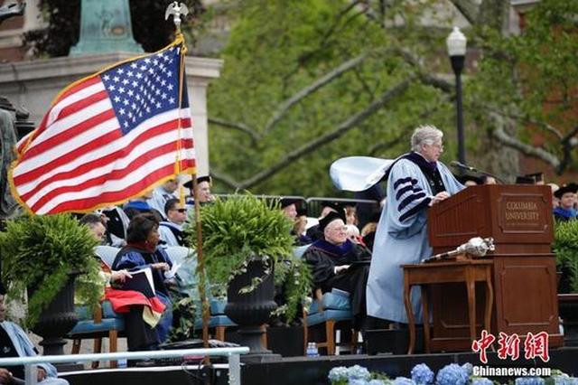 美国哥伦比亚大学校长布林格讲话时学位服和星条旗被风吹起。