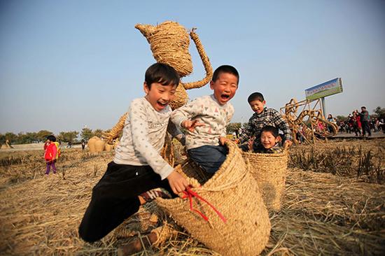 江苏泗洪，孩子们在稻米文化节的稻草人艺术展展区快乐地玩耍。视觉中国 资料