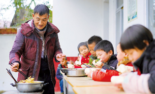 烧完饭菜后，章站亮给学校的学生们盛菜（1月3日摄）。