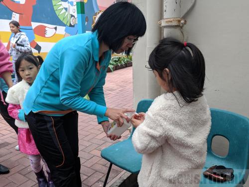 有老师在学校门外为小朋友和家长用酒精洗手液消毒双手。图片来源：香港电台网站/陈青仪 摄