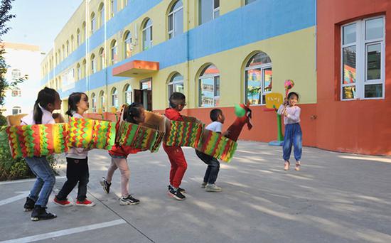 幼儿园小朋友用旧纸箱制成的舞龙服装玩耍。