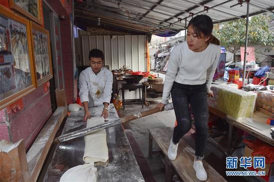 1月3日，郭炜兰（右）骑在一根1米多长、碗口粗的擀面杖上，上下跳动，用身体的力量将另一端的面团压成扁条形，这就是“骑木杖”擀面。