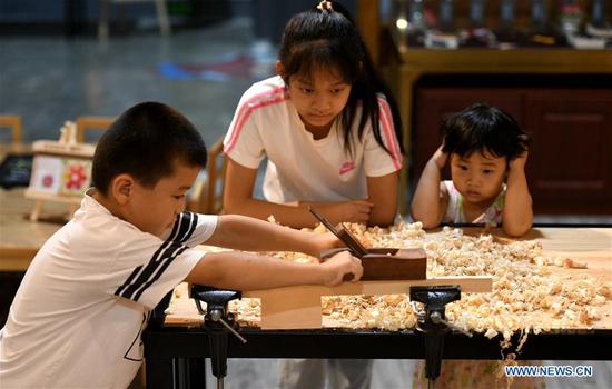 Children try to make woodwork in a cultural industry zone in Qiaoxi District of Shijiazhuang City, north China's Hebei Province, Aug. 10, 2020. Qiaoxi has organized a series of activities to enrich children's summer vacation and promote the intangible cultural heritages. (Photo by Xu Jianyuan/Xinhua)