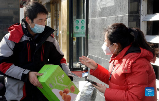 Courier Zhu Wenjun (L) talks with a customer in Xi'an, capital of northwest China's Shaanxi Province, Jan. 13, 2022. Postal and express delivery services in Xi'an have been gradually resumed in an orderly manner with strengthened epidemic prevention measures amid the latest resurgence. (Photo by Zou Jingyi/Xinhua)