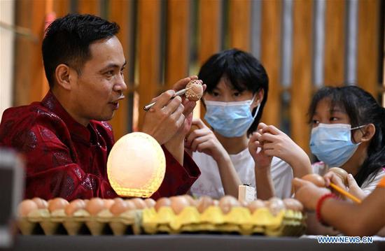 An artisan teaches children eggshell carving in a cultural industry zone in Qiaoxi District of Shijiazhuang City, north China's Hebei Province, Aug. 10, 2020. Qiaoxi has organized a series of activities to enrich children's summer vacation and promote the intangible cultural heritages. (Photo by Xu Jianyuan/Xinhua)