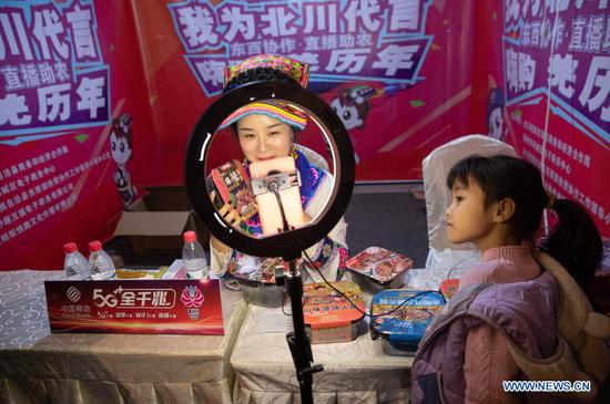 A child watches a livestreamer selling local products in Beichuan County, southwest China's Sichuan Province, Nov. 14, 2020. A live streaming event featuring poverty alleviation products was inaugurated here Saturday and lasts until Nov. 16. About 17,000 orders worth two million yuan (302,800 U.S. dollars) were reached during the two-hour livestream on Saturday. (Xinhua/Jiang Hongjing)