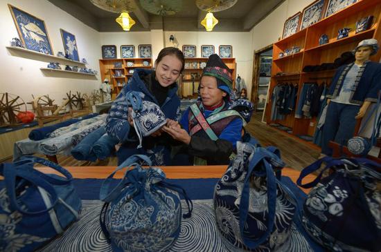 A sales assistant (L) and a resident relocated from a poverty-stricken area observe a batik product at a batik workshop in Danzhai County of Guizhou Province in southwest China, Dec. 1, 2020. (Xinhua/Yang Ying)