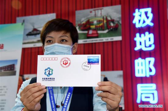 A staff member displays the first-day cover of the 2020 East Asia Marine Expo in Qingdao, east China's Shandong Province, Sept. 22, 2020. The 2020 East Asia Marine Expo opened Tuesday in Qingdao, a coastal city of east China's Shandong Province, convening more than 770 companies and institutes from over 70 countries and regions. More than 50,000 different exhibits ranging from ocean engineering, offshore oil and gas exploration, seabed exploration, deep-sea aquaculture and scientific research equipment, to scientific achievements in marine surveying and mapping as well as fishery products have been put on show at the six-day expo, which boasts 60,000 square meters of exhibition area. (Xinhua/Li Ziheng)