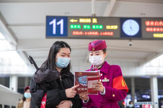 A staff member distributes epidemic prevention leaflets to a passenger at Chongqingbei Railway Station in Chongqing, southwest China, Jan. 25, 2021. The prevention and control efforts against the COVID-19 epidemic are strengthened at railway stations in Chongqing to protect the safety of passengers. (Xinhua/Huang Wei) 