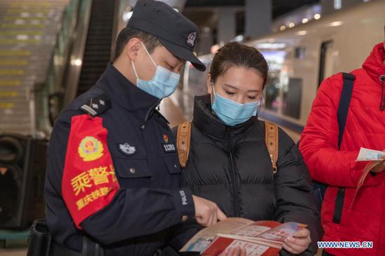 A police officer distributes epidemic prevention leaflets to passengers at Chongqingbei Railway Station in Chongqing, southwest China, Jan. 25, 2021. The prevention and control efforts against the COVID-19 epidemic are strengthened at railway stations in Chongqing to protect the safety of passengers. (Xinhua/Huang Wei)