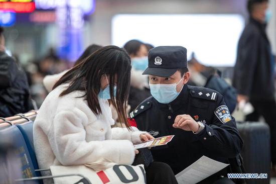 A police officer distributes epidemic prevention leaflets to a passenger at Chongqingbei Railway Station in Chongqing, southwest China, Jan. 25, 2021. The prevention and control efforts against the COVID-19 epidemic are strengthened at railway stations in Chongqing to protect the safety of passengers. (Xinhua/Huang Wei)