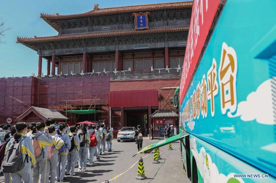 Tourists walk past a mobile COVID-19 vaccination vehicle outside the Donghua Gate of the Palace Museum in Beijing, capital of China, April 13, 2021. The bus-like facilities, equipped with vaccination stations, medical refrigerators and first-aid equipment, have been rolled out in different districts of Beijing to save time and improve inoculation efficiency. (Xinhua/Zhang Yuwei)