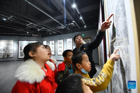 Wei Sancai (back) tells his experiences to students at his art exhibition in an art museum of Liuzhou City, south China's Guangxi Zhuang Autonomous Region, Dec. 5, 2021. An art exhibition of Wei Sancai, an art teacher, was unveiled on Friday in Liuzhou, displaying 100 art works on the theme of poverty alleviation and rural revitalization created by Wei during his tenure as a poverty alleviation official in Damiao Mountain. When he was assigned to Gaoqiang Village in Rongshui Miao Autonomous County of Liuzhou, Wei recorded the changes of the village with his paintings. In his spare time, he also took advantages of his profession to offer art classes for local children, providing them an access to the knowledge of arts. (Xinhua/Huang Xiaobang) 