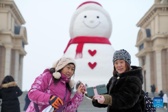 Tourists pose for photos with a huge snowman on the riverbank of Songhua River in Harbin, capital of northeast China's Heilongjiang Province, Jan. 9, 2022. The giant snowman is about 18 meters tall and 13 meters wide, using more than 2,000 cubic meters of snow. (Xinhua/Wang Jianwei)